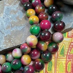 May include: A strand of multi-coloured round beads with shades of green, red, yellow, and white. The beads are made of polished stone and have a glossy finish.