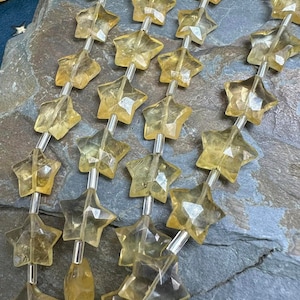 Puede incluir: Una hebra de cuentas de piedra preciosa amarilla en forma de estrella enhebradas en alambre plateado. Las cuentas son facetadas y tienen una apariencia translúcida.