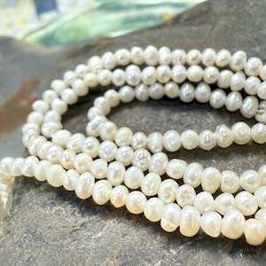 Puede incluir: Un collar de perlas blancas, dispuestas en forma circular sobre una superficie de piedra gris.