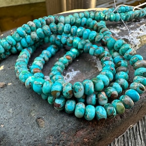 May include: A strand of turquoise blue beads with brown and white marbling. The beads are round and have a smooth, polished finish.