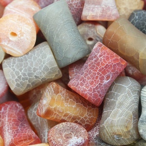 May include: A collection of agate beads in various colours and patterns, including red, orange, brown, and grey. The beads are smooth and polished, with a natural, organic look.