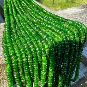 May include: A strand of green gemstone beads, likely peridot, with a faceted finish. The beads are strung on a white cord and are arranged in a fan shape.
