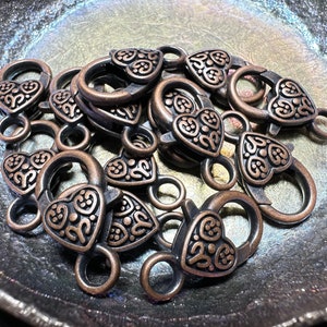 Puede incluir: Un montón de cierres en forma de corazón de bronce antiguo con diseños intrincados. Los cierres son perfectos para agregar un toque de encanto vintage a joyas, bolsos u otras artesanías.
