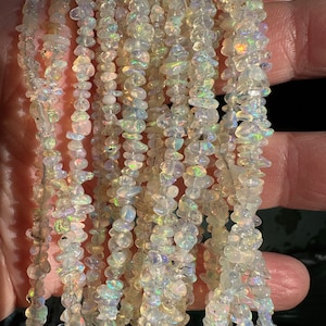May include: A strand of iridescent white opal chip beads. The beads are small and irregular in shape, with a translucent, glassy appearance. The strand is approximately 18 inches long.