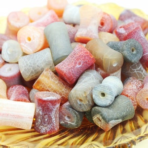 May include: A collection of agate beads in various shades of red, orange, and grey. The beads are all cylindrical and have a rough, textured surface.