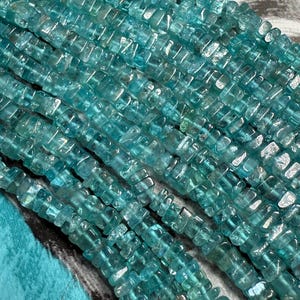 May include: A strand of light blue aquamarine gemstone beads. The beads are faceted and have a rectangular shape. The beads are strung on a clear thread.