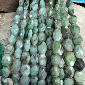 Puede incluir: Hebras de cuentas de esmeralda facetadas en varios tonos de verde y turquesa. Las cuentas están ensartadas, creando un efecto de cascada. Las piedras preciosas tienen una superficie pulida, mostrando su belleza natural.