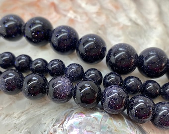 May include: A strand of dark blue gemstone beads with a speckled, starry appearance. The beads are round and smooth, and they are arranged in a loose, flowing pattern.