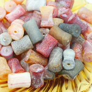 May include: A collection of colourful agate beads in various shades of red, orange, brown, and grey. The beads are smooth and polished, with a natural, organic look. They are perfect for jewellery making or other craft projects.
