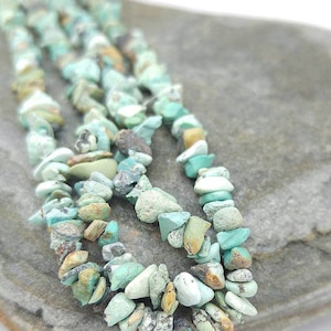 May include: A strand of turquoise chip beads in various shades of blue and green. The beads are irregular in shape and size, and have a rough, natural texture.