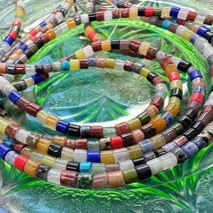 May include: A close-up of a multi-coloured assortment of gemstone beads. The beads are round and have a variety of colours, including red, orange, yellow, green, blue, and purple. The beads are arranged in a circular pattern, and they are all strung together on a string.