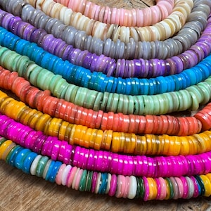 Può includere: Primo piano di perline rotonde e piatte colorate in un arcobaleno di colori. Le perline sono disposte in file curve, mostrando sfumature di rosa, viola, blu, verde, arancione, giallo e bianco. Ideale per la creazione di gioielli.