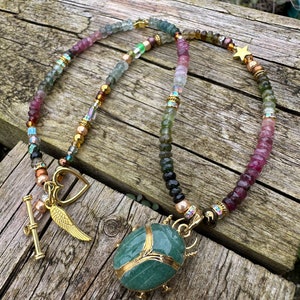 May include: A multi-colored beaded necklace with a green stone beetle pendant, gold accents, and charms including a heart, wings, and a star.