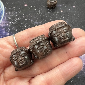 May include: Four small, dark brown wooden Buddha head sculptures. The sculptures are carved with intricate details and have a serene expression.