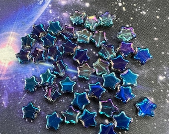 May include: Iridescent star-shaped beads in blue, purple, and green hues. The beads are scattered on a dark background with a galaxy design. These beads are suitable for jewellery making and crafting projects, adding a celestial touch to designs.