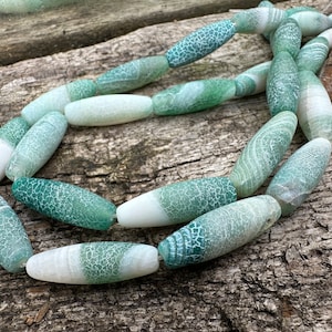 May include: A strand of green and white agate beads. The beads are oval shaped and have a mottled pattern.