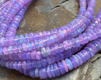 May include: A strand of iridescent purple opal beads. The beads are small and round, and they have a smooth, polished finish. The beads are strung on a clear thread.