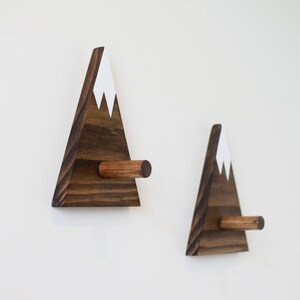 May include: Two wooden mountain-shaped wall hooks with a white painted snow cap and a brown wooden peg.