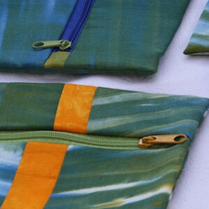 Könnte beinhalten: Drei grüne, blaue und orangefarbene Stoffbeutel mit Reißverschlüssen. Die Beutel sind aus einem weichen, gemusterten Stoff gefertigt und haben einen Batik-Effekt.