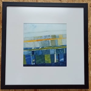 Könnte beinhalten: Ein gerahmtes abstraktes Kunstwerk mit einem Patchwork aus blauem, grünem und gelbem Stoff. Der Stoff ist in horizontalen Bändern angeordnet, mit einem dünnen gelben Band, das durch die Mitte verläuft.