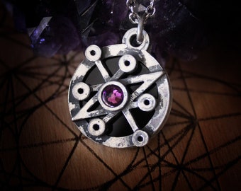May include: A silver pendant necklace with a circular design featuring a six-pointed star with a purple gemstone in the centre. The pendant is on a silver chain.