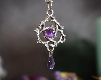 May include: Silver pendant necklace with a purple amethyst gemstone set in a thorny, intricate design. A small purple crystal dangles from the bottom.