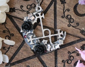 May include: Silver pendant necklace featuring a crescent moon with black roses and a pentagram with crosses. The pendant is on a wooden surface with a black and white star design. The text "HANDMADE IN FRANCE" is visible in a circle.