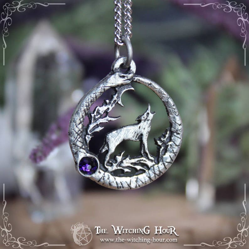 Puede incluir: Collar con colgante de plata que representa un lobo aullando a la luna, rodeado de una serpiente y follaje. El colgante tiene un acento de piedra preciosa p&uacute;rpura.