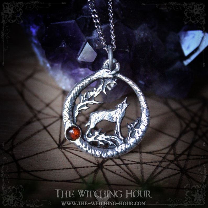 Puede incluir: Collar con colgante de plata que representa un lobo aullando a la luna, rodeado de una serpiente y follaje. El colgante tiene un acento de piedra preciosa &aacute;mbar.