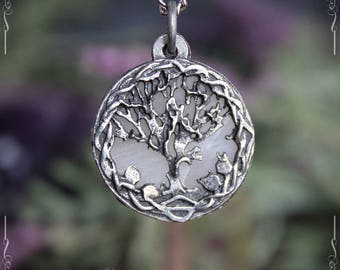 May include: A silver pendant necklace featuring a tree of life design with a white stone in the center. The pendant is round and has a Celtic knot border.