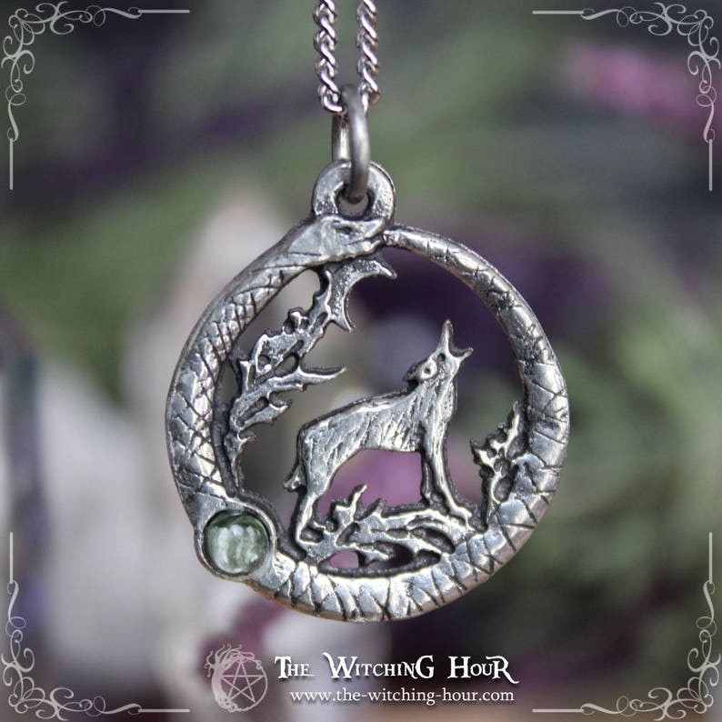 Puede incluir: Collar con colgante de plata que representa un lobo aullando a la luna, rodeado de una luna creciente y follaje. El colgante tiene un acento de piedra preciosa verde.