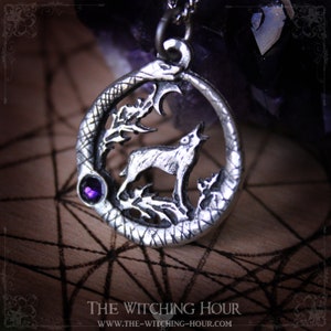 Puede incluir: Collar con colgante de plata que representa un lobo aullando a la luna, rodeado de una serpiente y follaje. El colgante tiene una peque&ntilde;a piedra preciosa p&uacute;rpura.