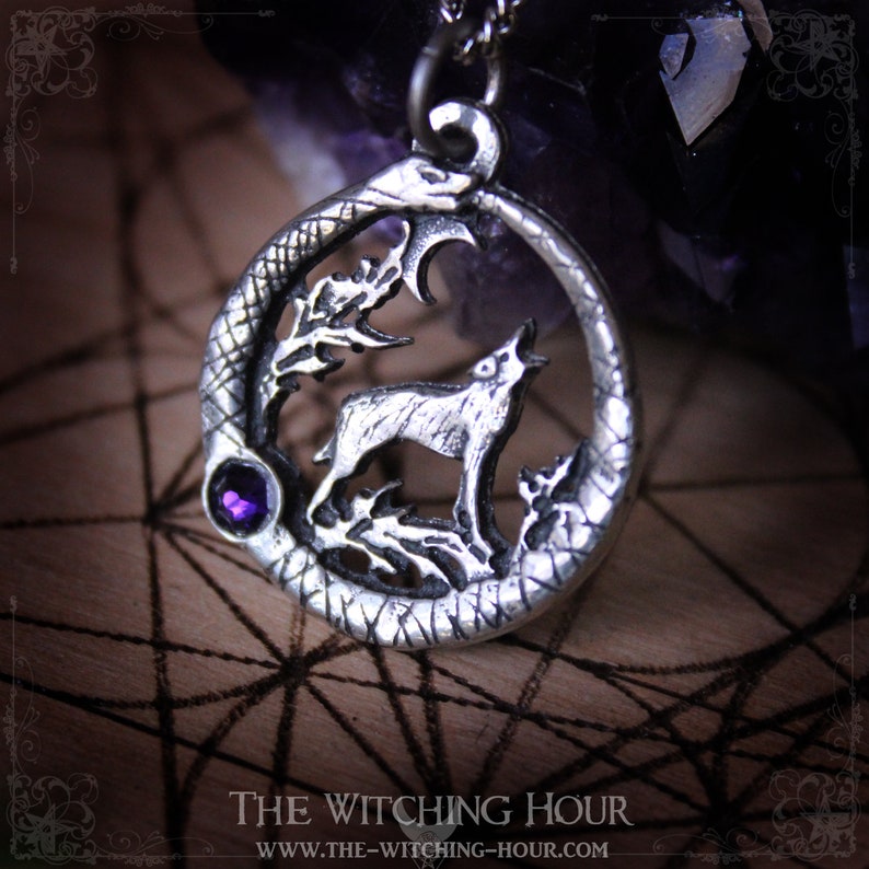 Puede incluir: Collar con colgante de plata que representa un lobo aullando a la luna, rodeado de una serpiente y follaje. El colgante tiene una peque&ntilde;a piedra preciosa p&uacute;rpura.