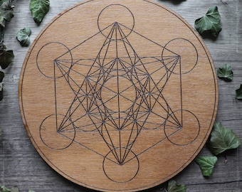 Könnte beinhalten: Eine runde Holzscheibe mit einem gravierten geometrischen Muster aus einem Stern, Kreisen und Linien. Das Muster ist ein heiliges geometrisches Muster, das als Metatrons Würfel bekannt ist.