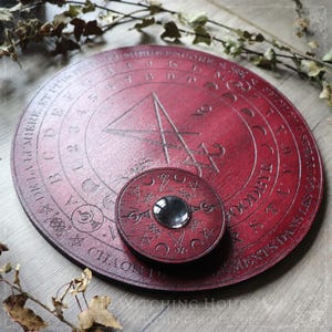 May include: A red wooden circular board with a black triangle and a smaller circular board with a mirror in the center. The board has the words "CHAOS" and "GODS" inscribed on it.