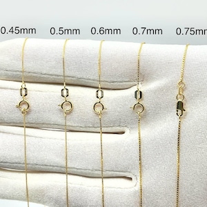 以下が含まれることがあります： 0.45mm、0.5mm、0.6mm、0.7mm、0.75mmとラベル付けされた、厚みの異なる5本のゴールドチェーン。各チェーンには小さな円形の引き輪と長方形のタグが付いています。チェーンは白い背景に対して垂直に並べられています。