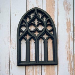 May include: Black wooden cutout of a gothic arch window with intricate details. The window is framed with a thick black border and has four smaller arches within the larger arch.