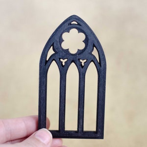 May include: Black wooden window frame cutout with a decorative design. The frame has three arched windows with a quatrefoil design at the top.