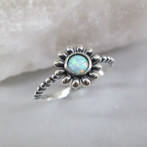 May include: A silver ring with a white opal gemstone set in a flower design. The band is twisted and has a beaded texture.