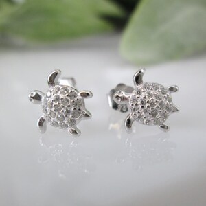 May include: A pair of silver turtle stud earrings with clear cubic zirconia stones.