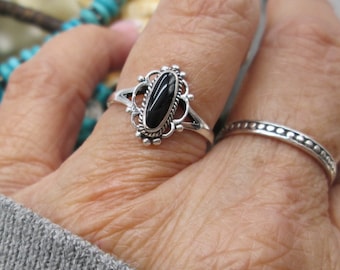 May include: A silver ring with a black oval gemstone set in a decorative filigree design.