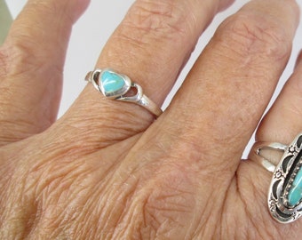 May include: Two silver rings with turquoise stones. One ring features a heart-shaped turquoise stone, while the other has an oval turquoise stone with decorative silver accents. The rings are displayed on a hand.