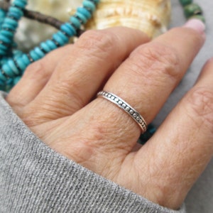 May include: A thin silver ring with a beaded edge. The ring is worn on a person's finger.