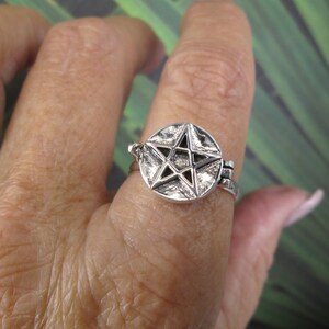 May include: A silver ring with a pentagram design. The ring is adjustable and has a hinged opening.