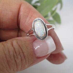 May include: A silver ring with an oval-shaped white opal gemstone set in a delicate, ornate silver bezel.