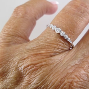 May include: A delicate silver band ring with a row of small, clear gemstones set in a curved design.