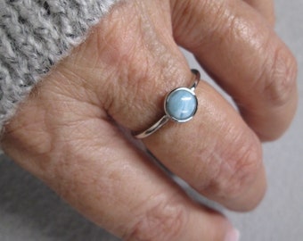 May include: A silver ring with a light blue gemstone. The ring is on a person's finger.