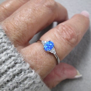 May include: A silver ring with a blue oval opal gemstone and smaller clear gemstones on the band.