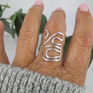May include: A silver ring with a unique, abstract design. The ring is made of a single piece of metal that is twisted and shaped into a series of loops and curves.