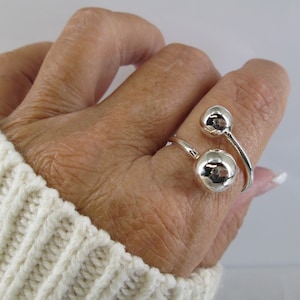 May include: A silver ring with two round balls. The ring is designed to wrap around the finger.